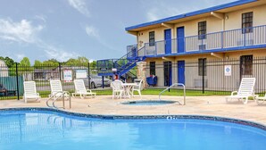 A pool area with lounge chairs and a building with a blue exterior and a balcony. - Rodeway Inn New Braunfels - San Antonio Area (New Braunfels)