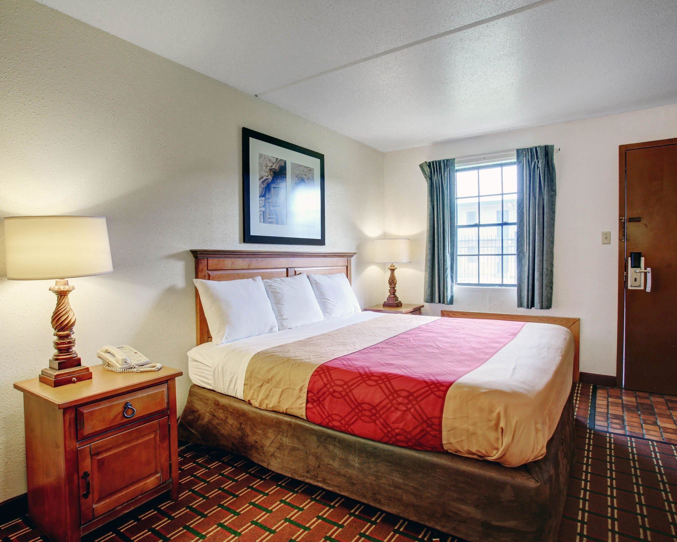 A hotel room with a bed, bedside tables, a telephone, a window with curtains, and a framed picture on the wall.