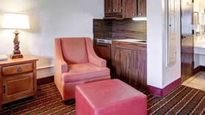 A compact hotel room with a kitchenette, a small sofa, a bedside table with a lamp, and a patterned carpet. - Rodeway Inn New Braunfels - San Antonio Area (New Braunfels)