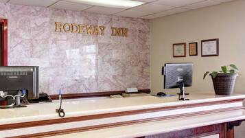 A reception desk at Rodeway Inn with a marble wall, a computer, a phone, and a potted plant.