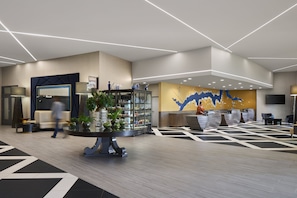 A modern lobby with a reception desk, seating area, and decorative plants.