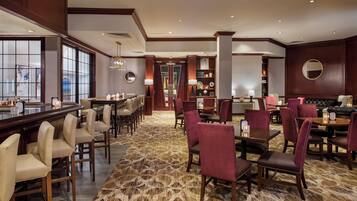 A hotel lobby with a bar area, seating arrangements, and a reception desk.