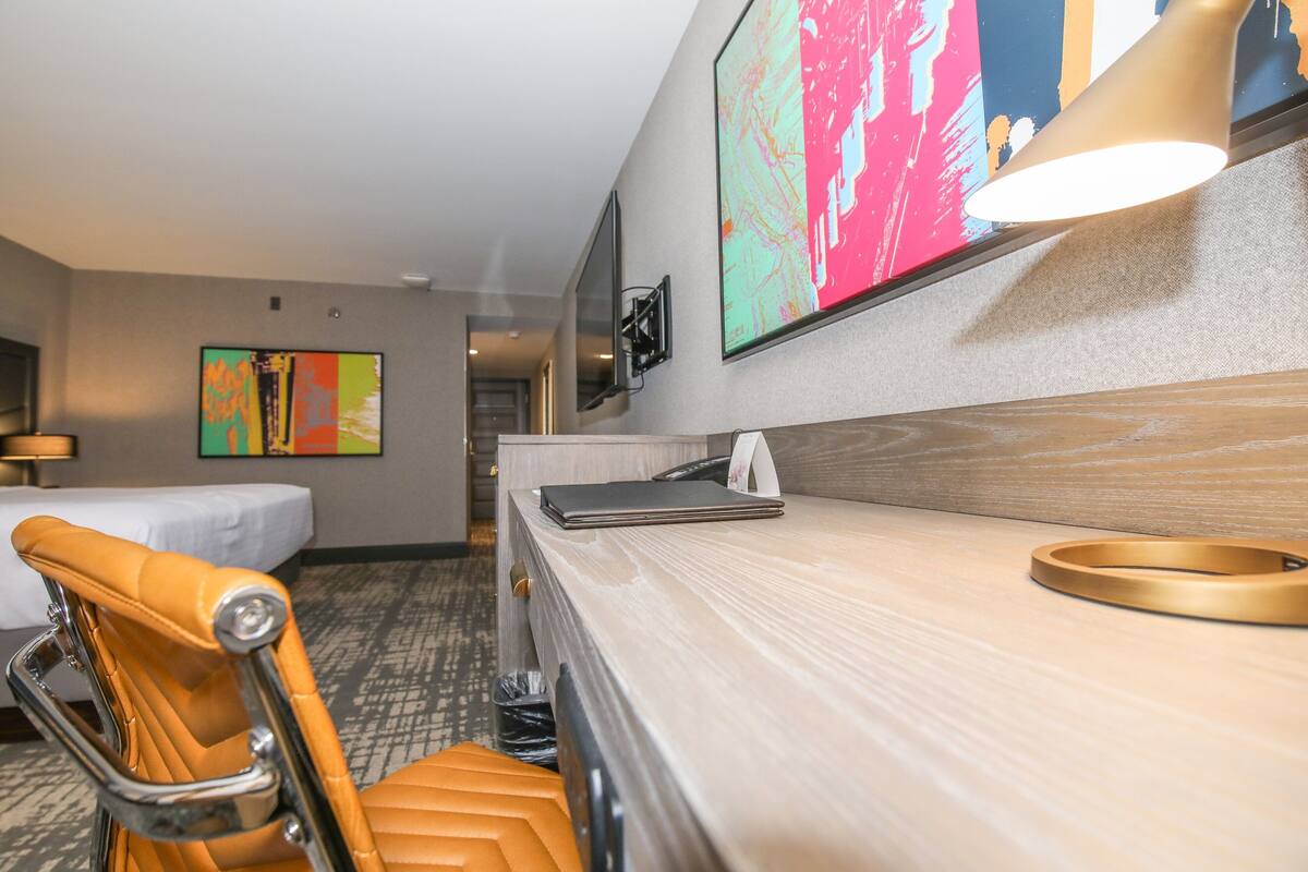Een hotelkamer met een bed, een bureau, een stoel, een televisie en kunst aan de muur.