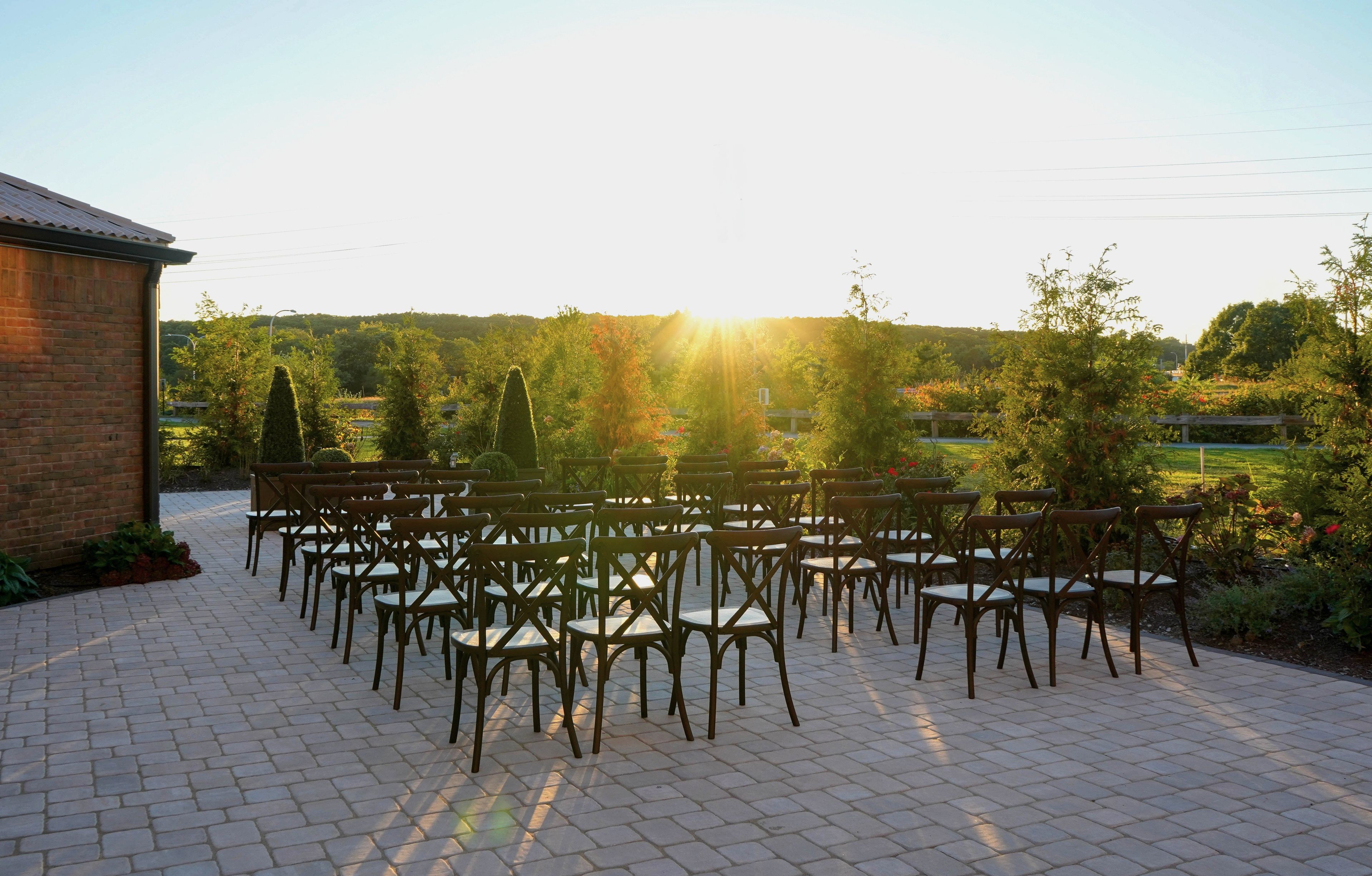 An outdoor seating area with chairs and tables arranged on a paved surface, surrounded by greenery and trees.
