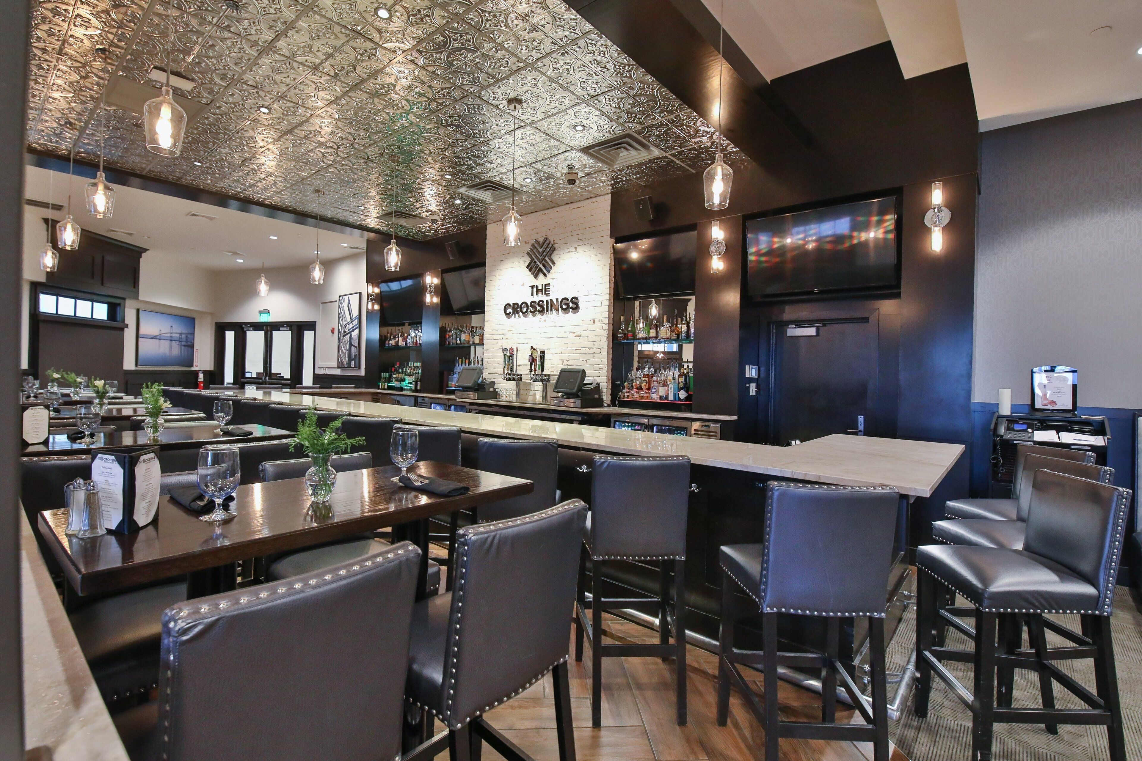 Interior de un restaurante con zona de bar, diversas disposiciones de asientos y un letrero destacando 'The Crossings'.