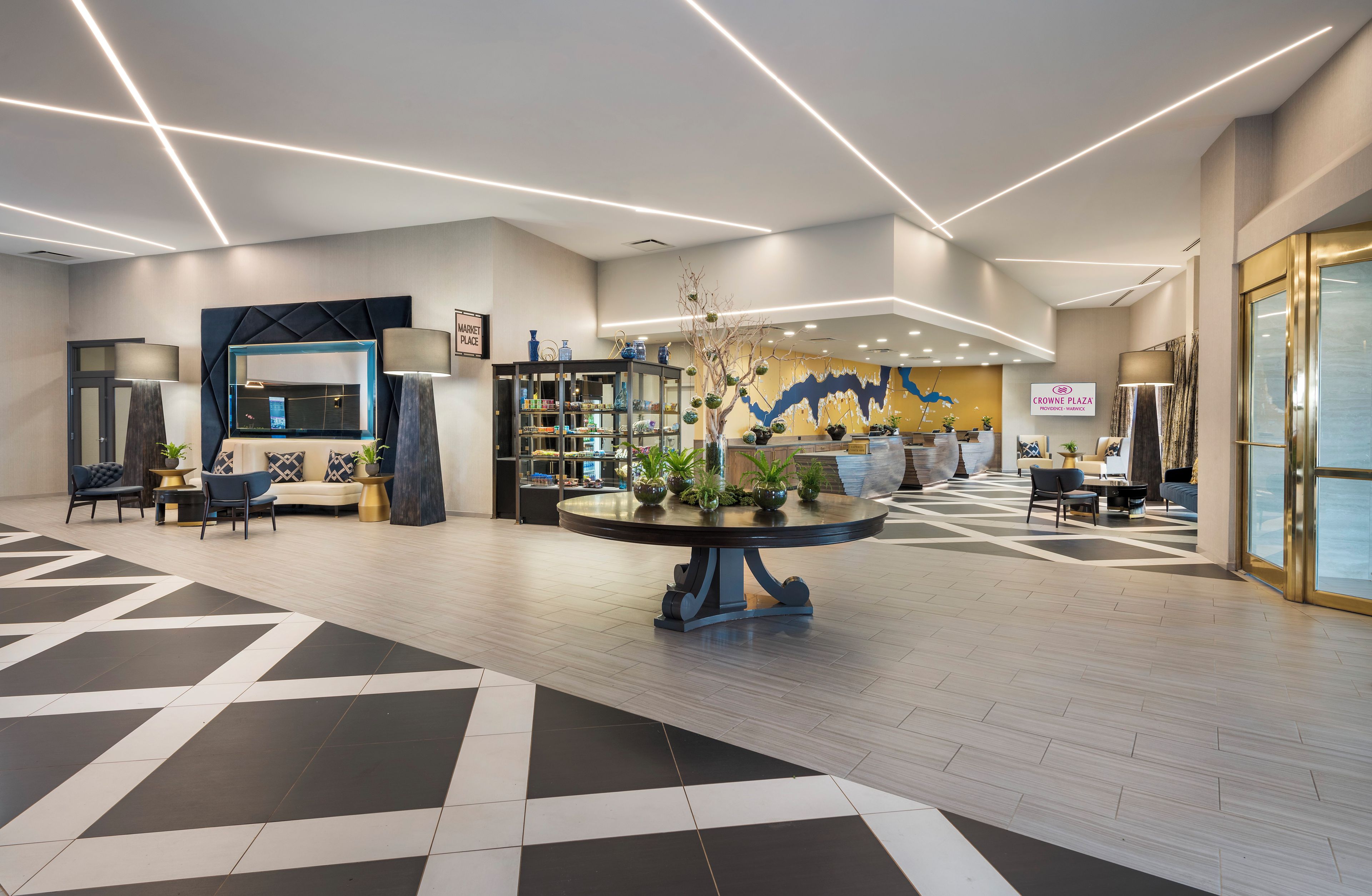 A modern lobby with a central round table, seating areas, and a large wall mural.