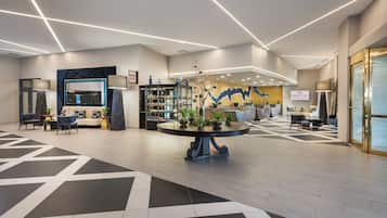 A modern lobby with a central round table, seating areas, and a large wall mural.