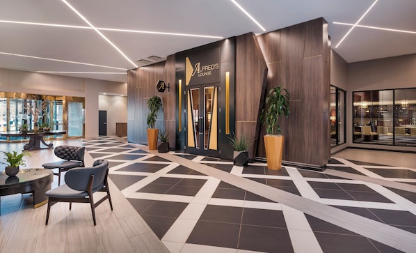 A modern lounge area with a checkered floor, seating, and potted plants.