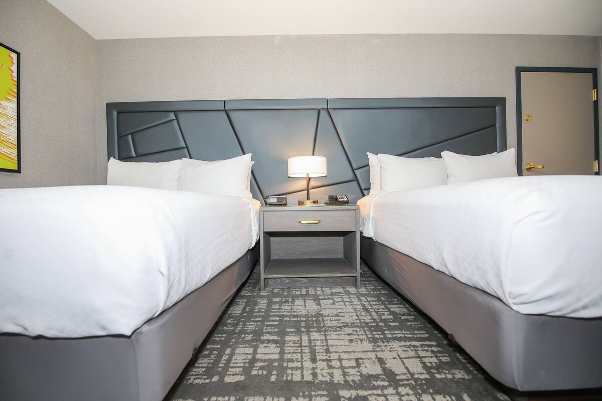 Een hotelkamer met twee bedden, een nachtkastje met een lamp en een kamerkleed met dessin.
