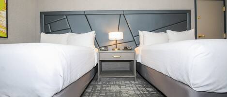 A hotel room with two beds, a nightstand with a lamp, and a patterned rug.