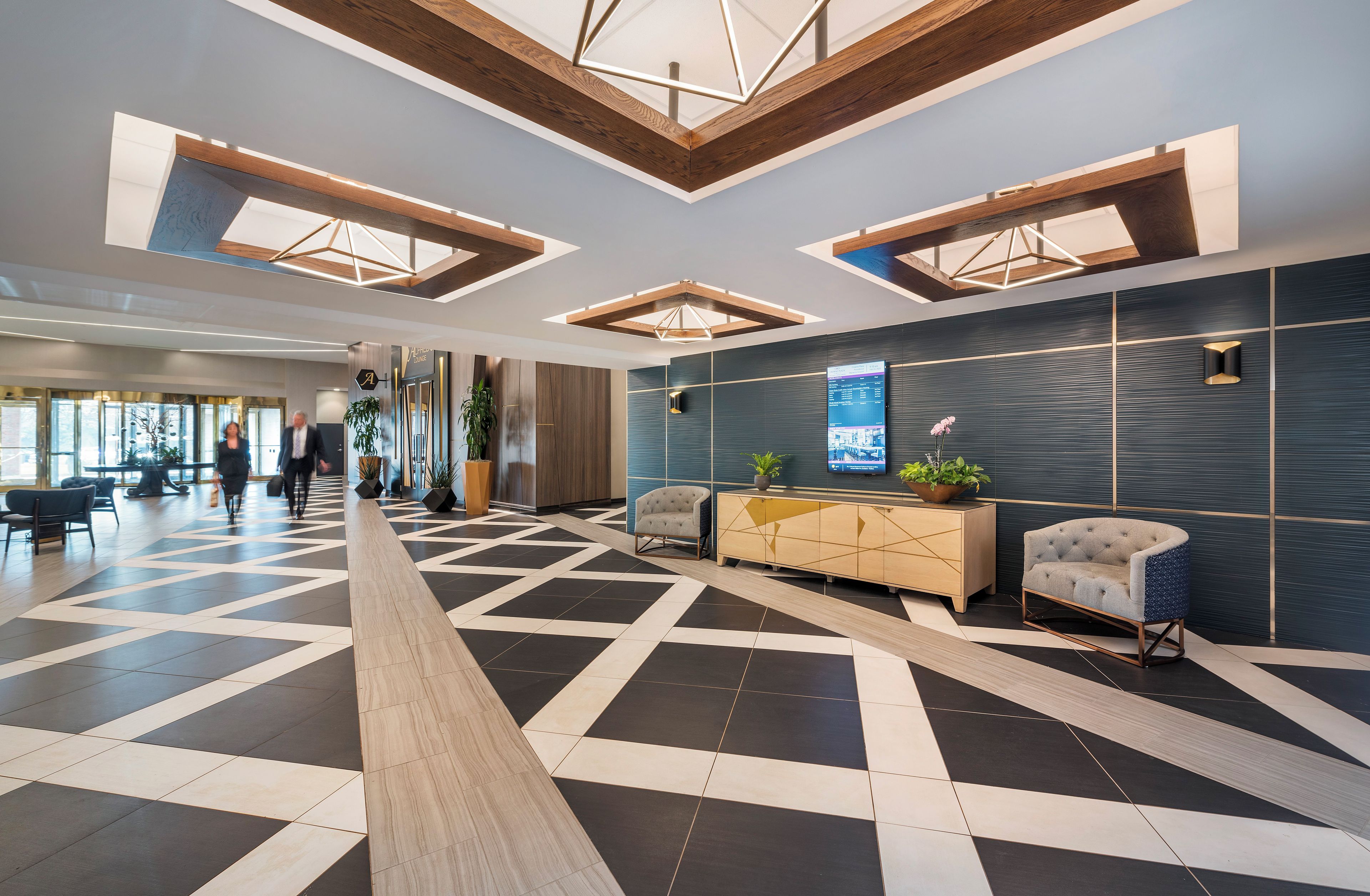 Un moderno vestíbulo de hotel con piso de diseño geométrico, un mostrador de recepción y una gran pantalla digital.