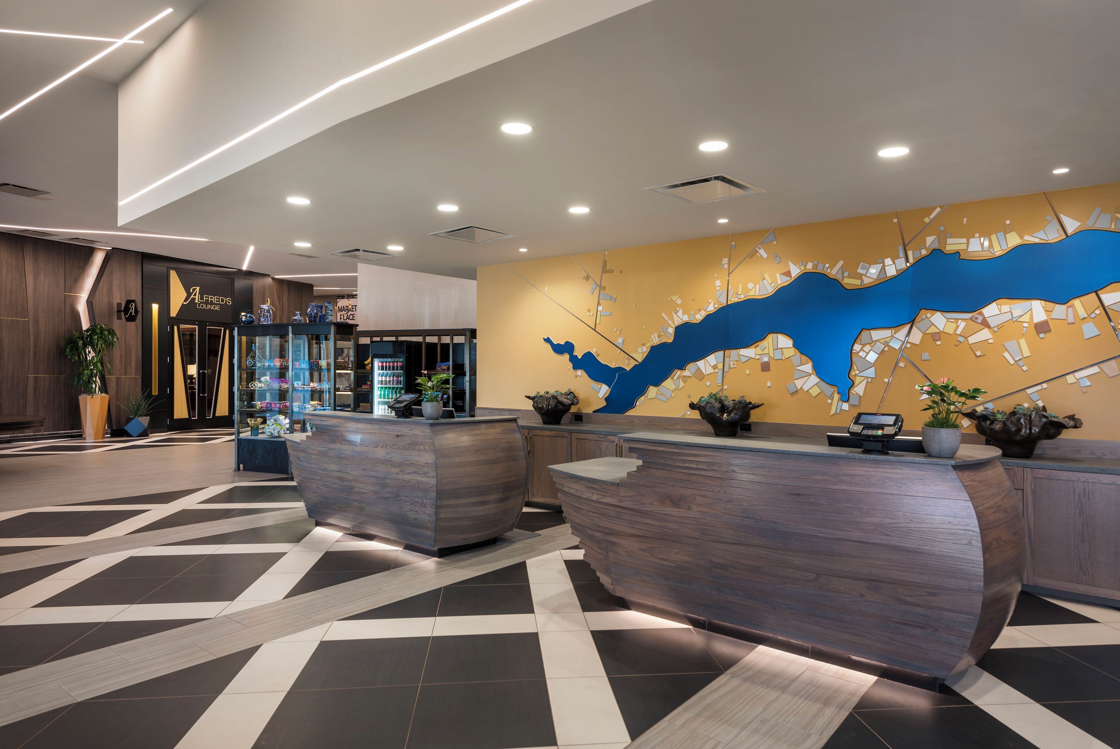 A modern lobby with a reception desk, a wall mural, and a coffee shop area.
