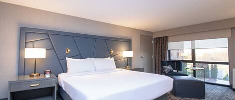 A hotel room with a large bed, two bedside tables with lamps, a small sofa, and a window with a view.