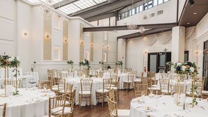 Un amplio salón de banquetes con mesas redondas, sillas doradas y manteles blancos.