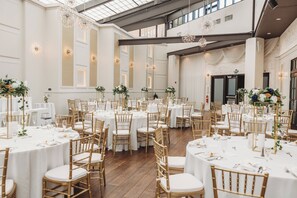 A spacious banquet hall with round tables, gold chairs, and white tablecloths.