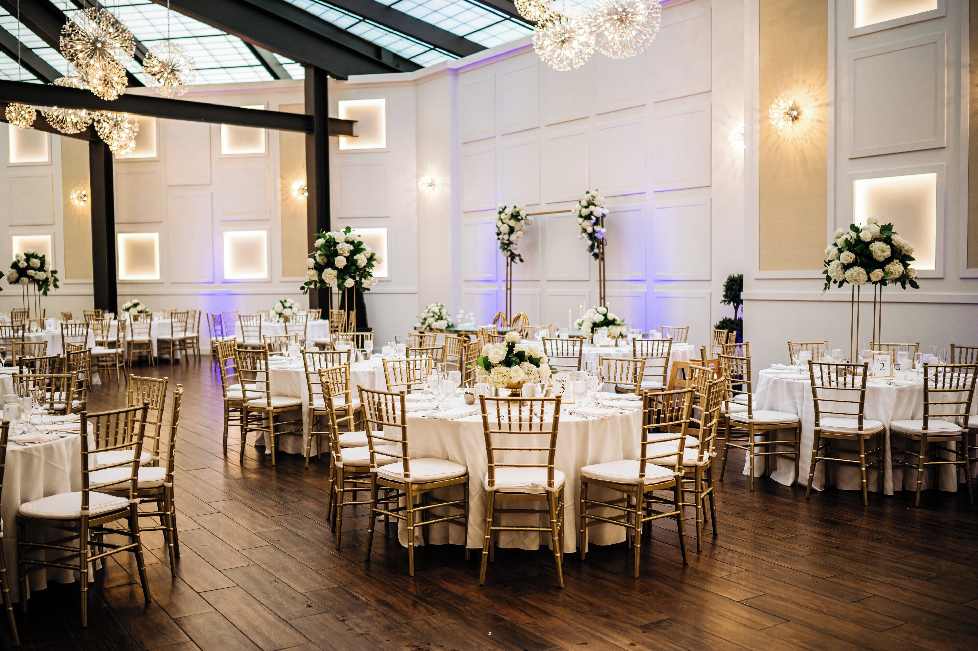 A banquet hall with round tables, gold chairs, and floral centerpieces.