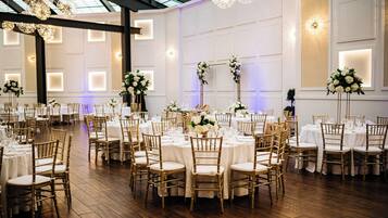A banquet hall with round tables, gold chairs, and floral centerpieces.