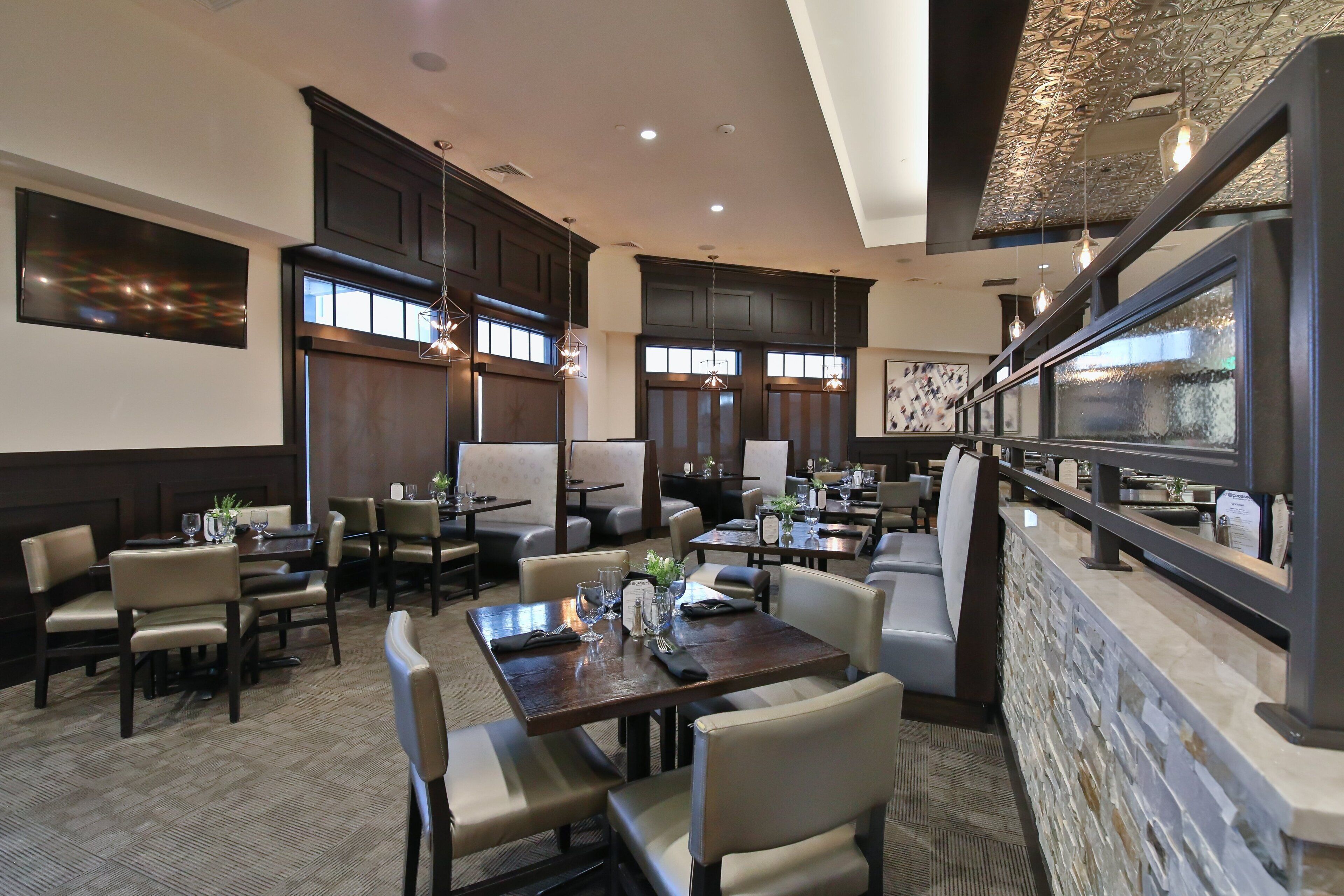 A spacious dining area with multiple tables and chairs, a stone accent wall, and a large window providing natural light.