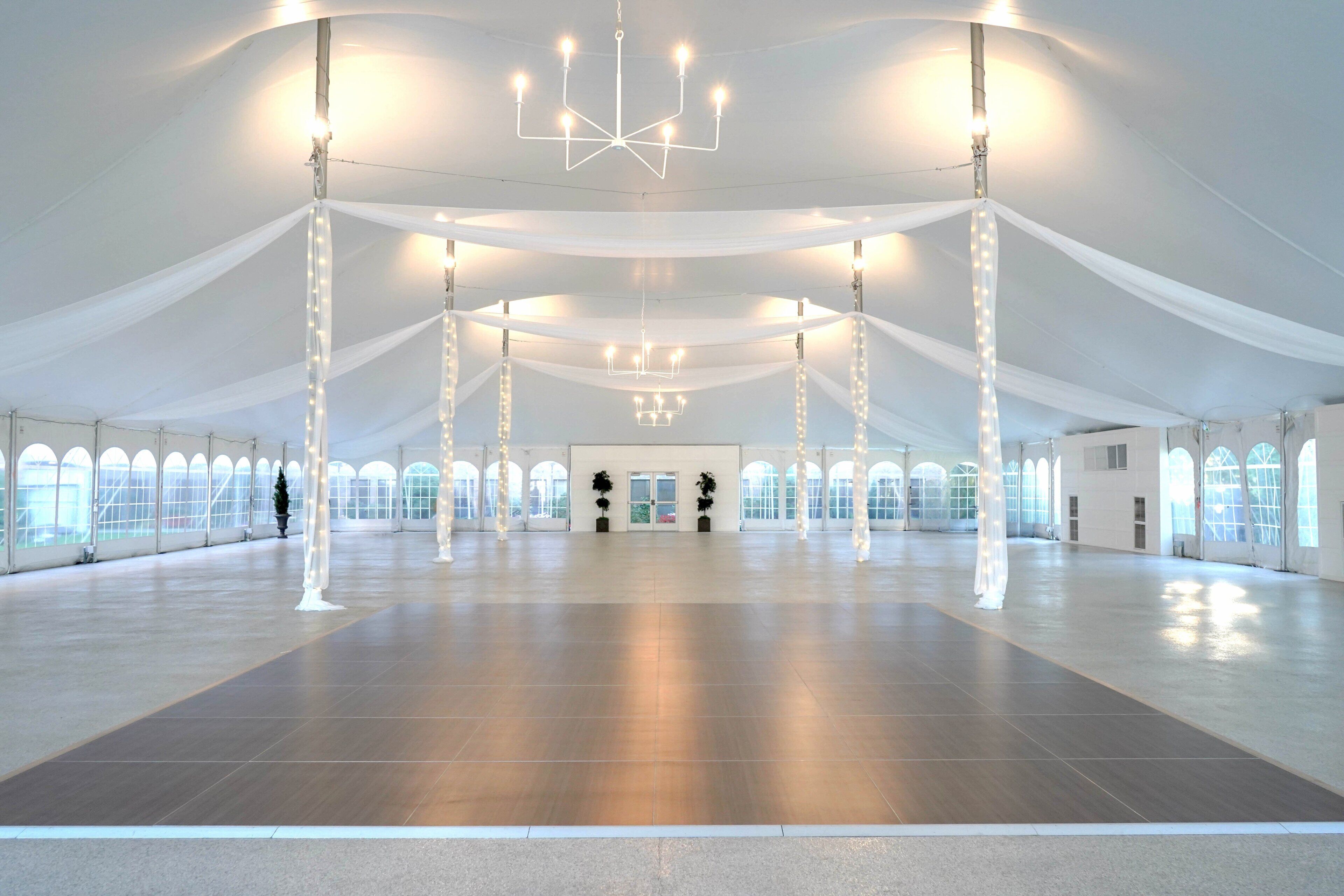 A large, open indoor space with high ceilings, white drapery, and multiple chandeliers.