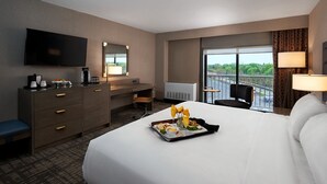 Habitación de hotel con cama, escritorio, silla, televisión y ventana con vistas a un estacionamiento y zonas verdes.