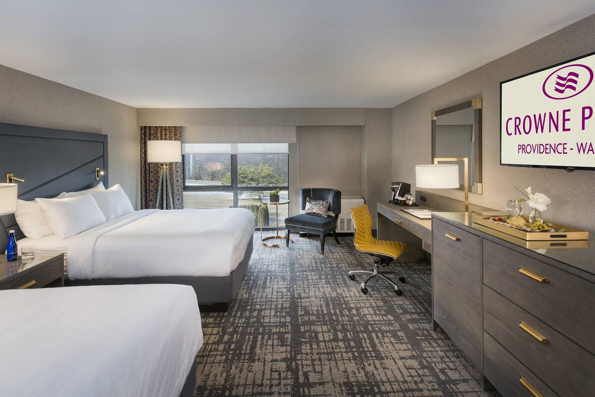 Hotelkamer met twee bedden, een bureau, een stoel, een kleine tafel met een lamp en een groot raam met uitzicht.