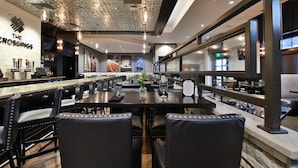 Een restaurantinterieur met een bar, zwarte leren stoelen en een plafond met een uniek patroon.