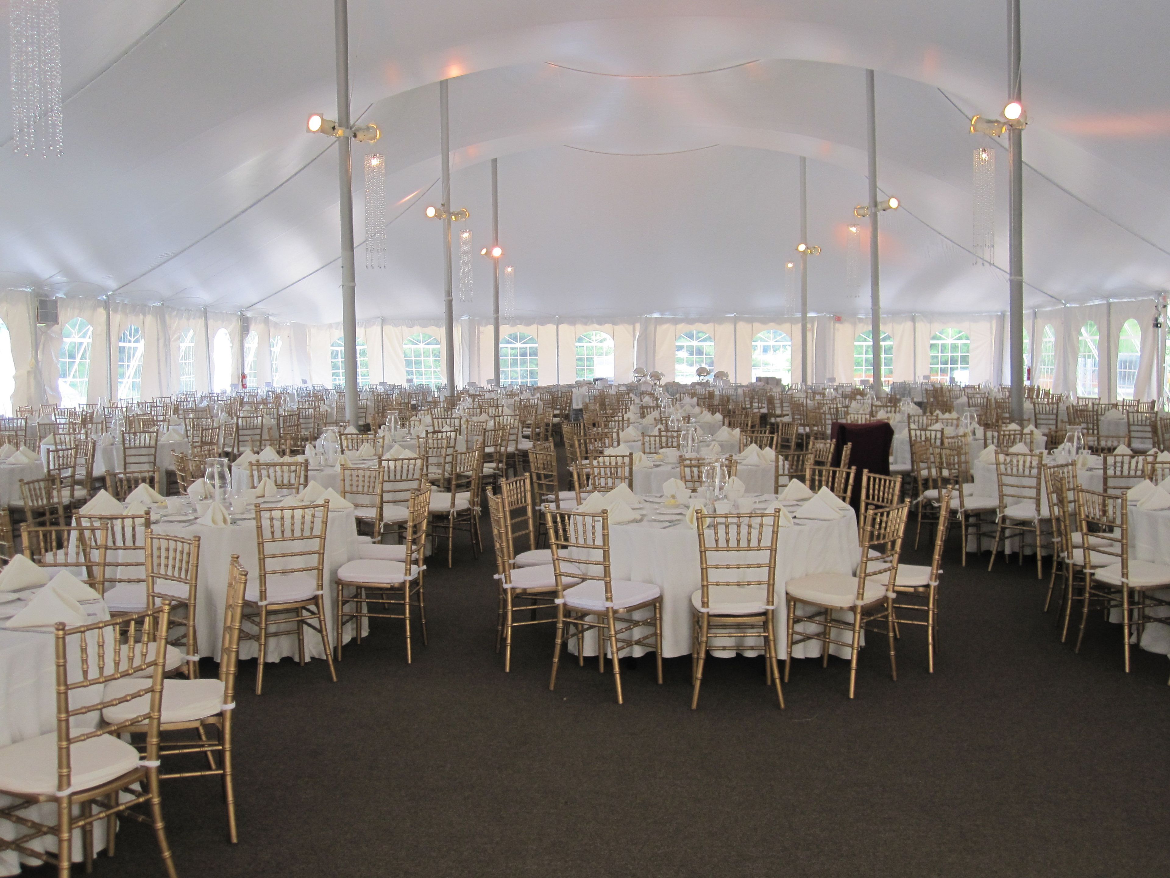Een ruime tent voor evenementen met rijen ronde tafels en stoelen, en een centrale gang.