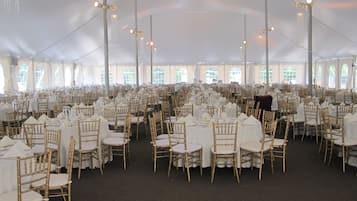 Een ruime tent voor evenementen met rijen ronde tafels en stoelen, en een centrale gang.