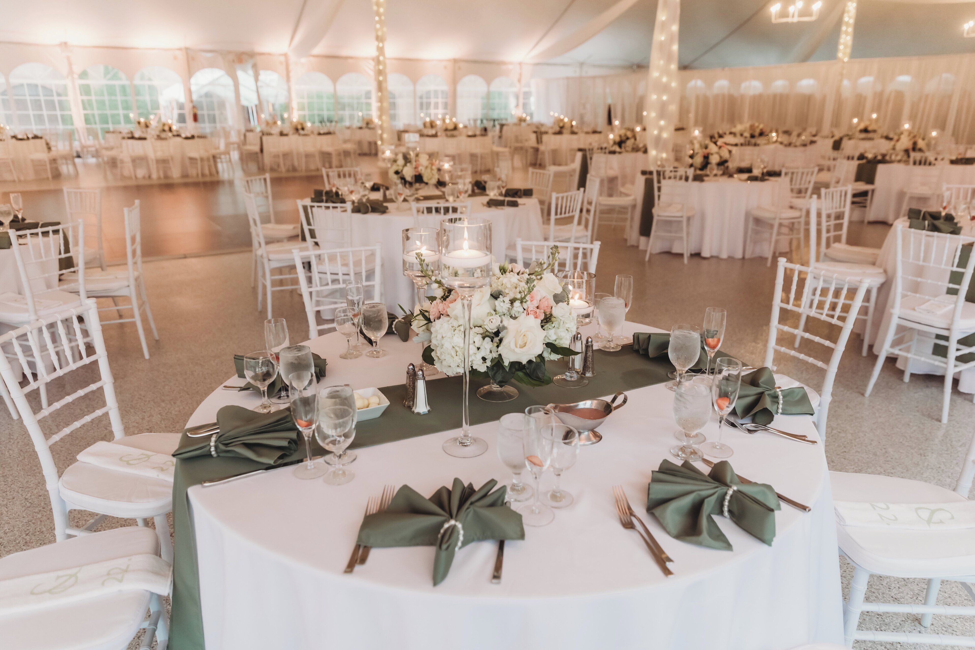 A tented wedding venue with round tables, white chairs, and floral centerpieces.