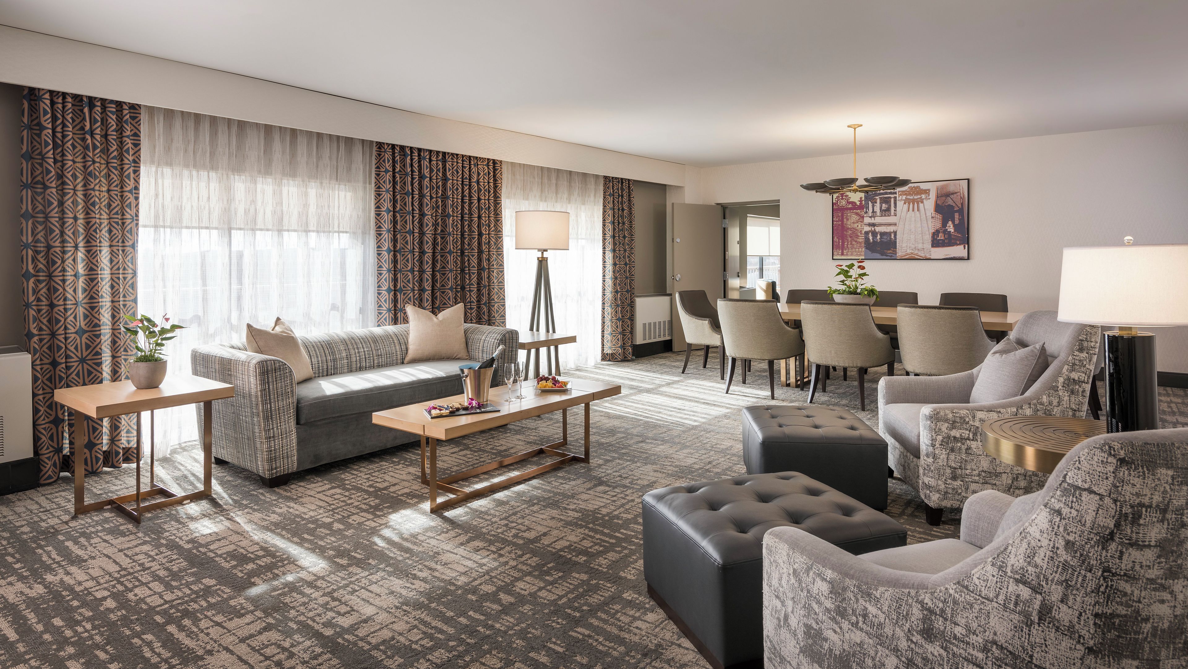A modern hotel room with a sofa, armchairs, a dining table, and a coffee table.