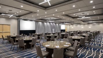 Un salón de conferencias con varias mesas y sillas, una pantalla grande y suelo alfombrado.