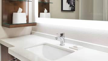 Un baño moderno con lavamanos doble, repisas de vidrio con artículos de aseo, un perchero y una obra de arte enmarcada en la pared.