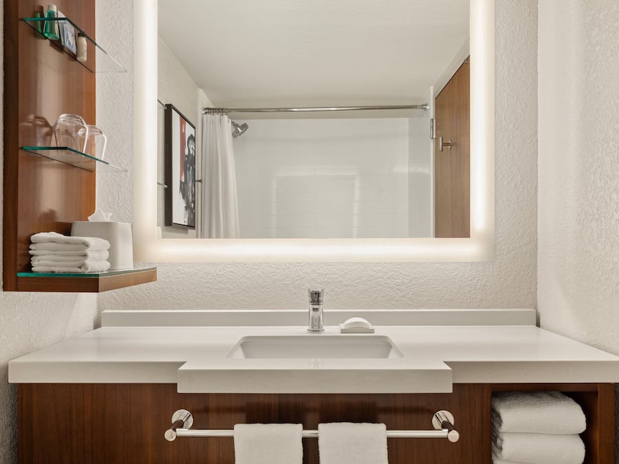 Un baño moderno con lavamanos blanco, tocador de madera y cabina de ducha con mampara de vidrio.
