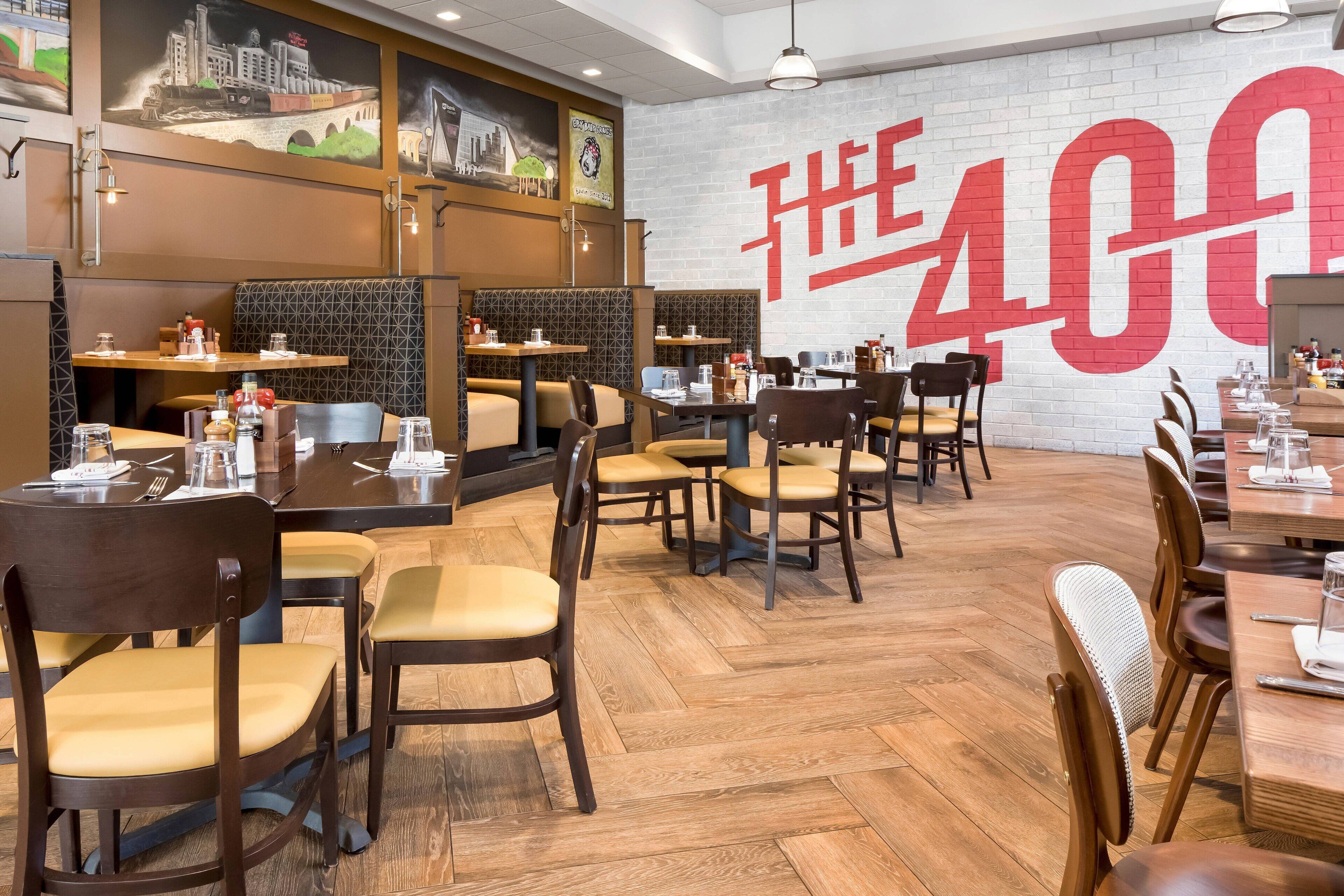 A restaurant with wooden flooring, multiple tables and chairs, and a large wall mural with a price sign.