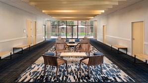A modern hotel lobby with a long corridor, wooden benches, a central seating area with tables and chairs, and large windows offering a view of the outdoors. - Delta Hotels by Marriott Minneapolis Northeast (Minneapolis)