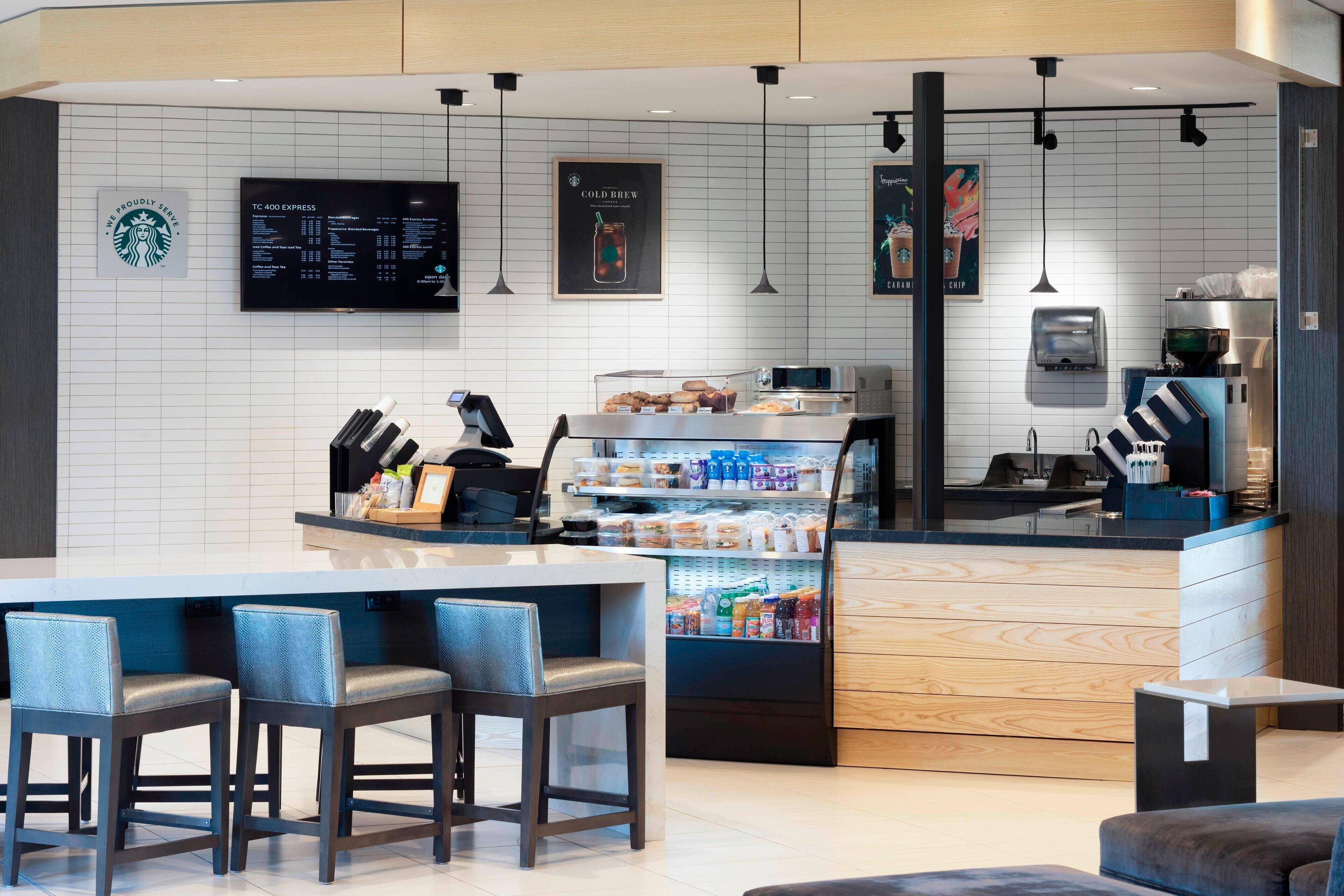 Interior de una cafetería moderna con mostrador, zona de asientos y exhibición de bebidas.