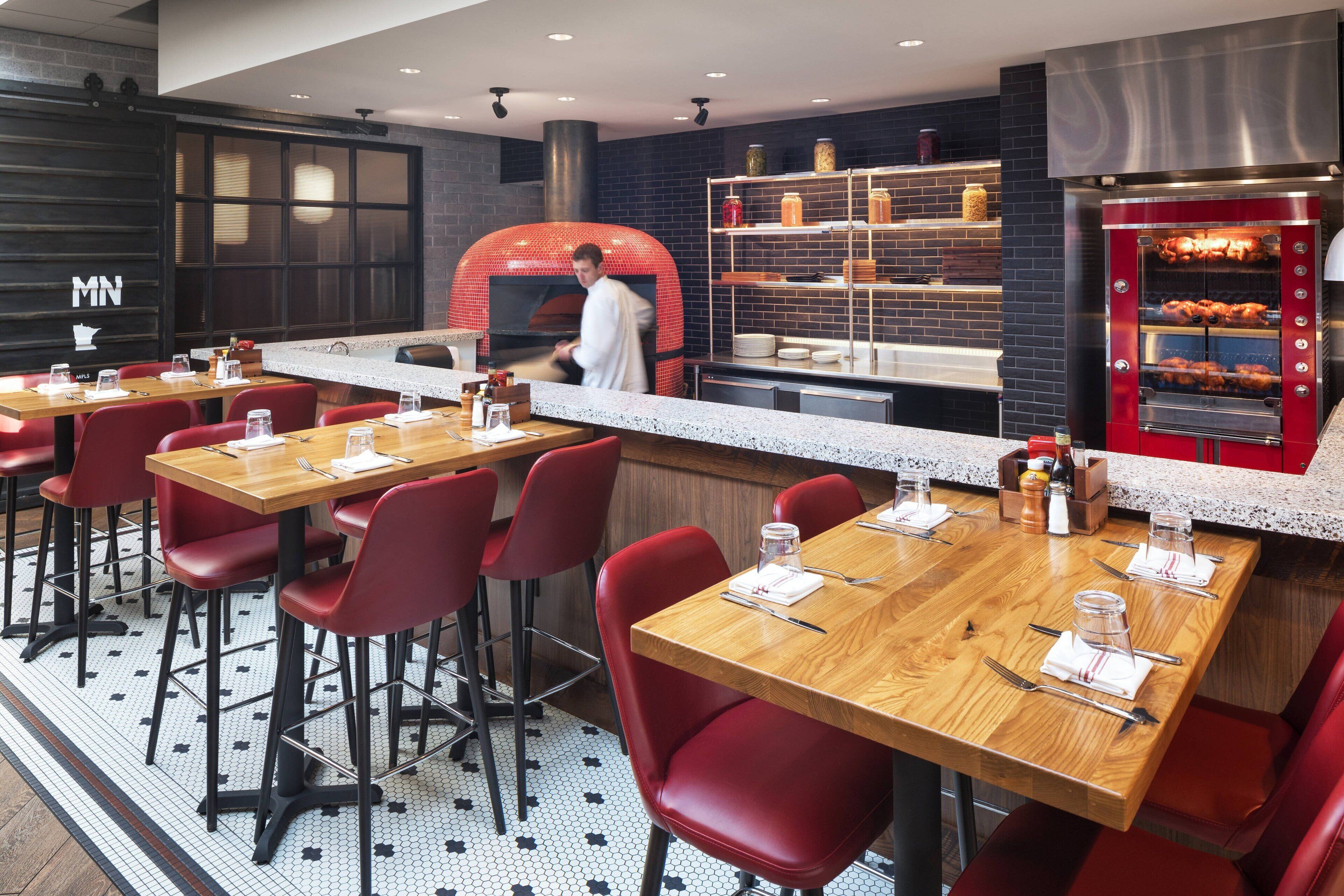 Un restaurante con mesas de madera, sillas rojas, una pared de ladrillo y un horno para pizza.