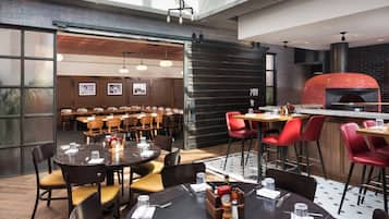 Un restaurante moderno con mesas redondas, sillas rojas y una pared de ladrillo.