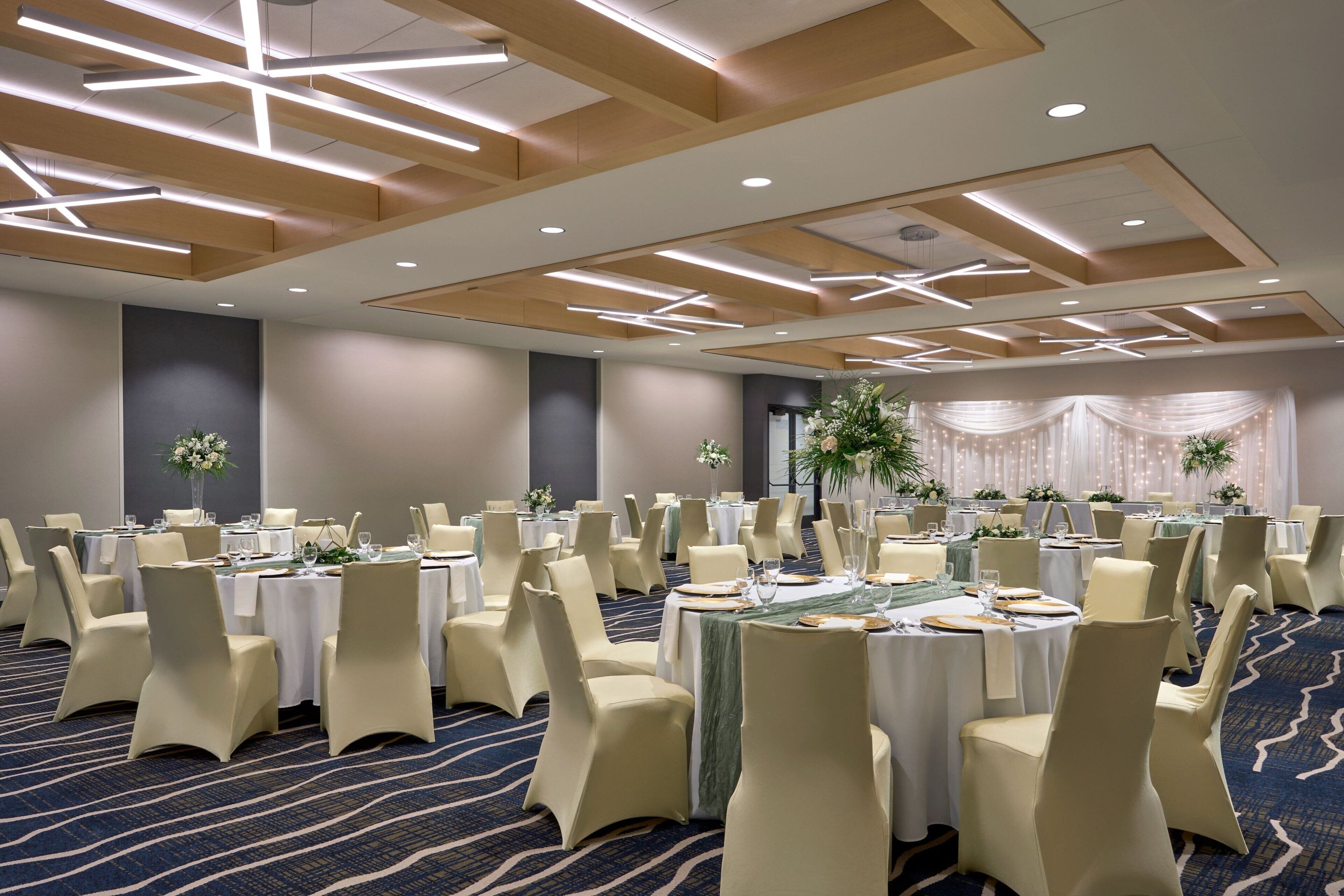 Une salle de banquet avec des tables rondes, des chaises de couleur beige et un sol recouvert de moquette.