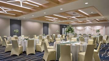 Une salle de banquet avec des tables rondes, des chaises de couleur beige et un sol recouvert de moquette.