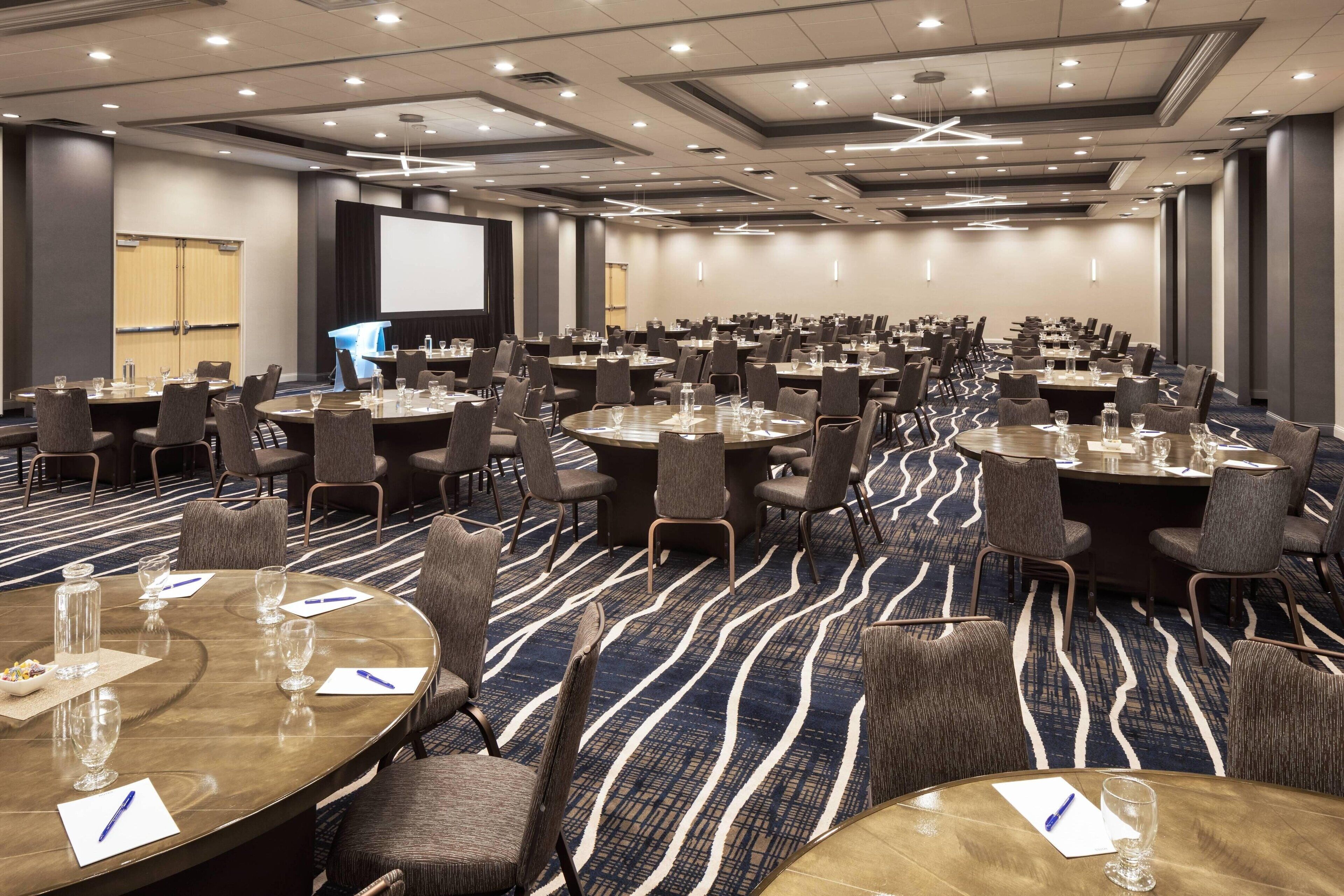 Une salle de conférence équipée de plusieurs tables rondes, de chaises et d’un grand écran.