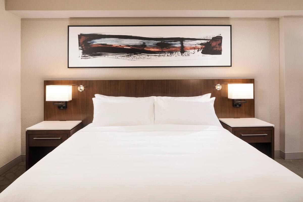 Una habitación de hotel con una cama grande, dos mesitas de noche y un cuadro abstracto colgado en la pared.
