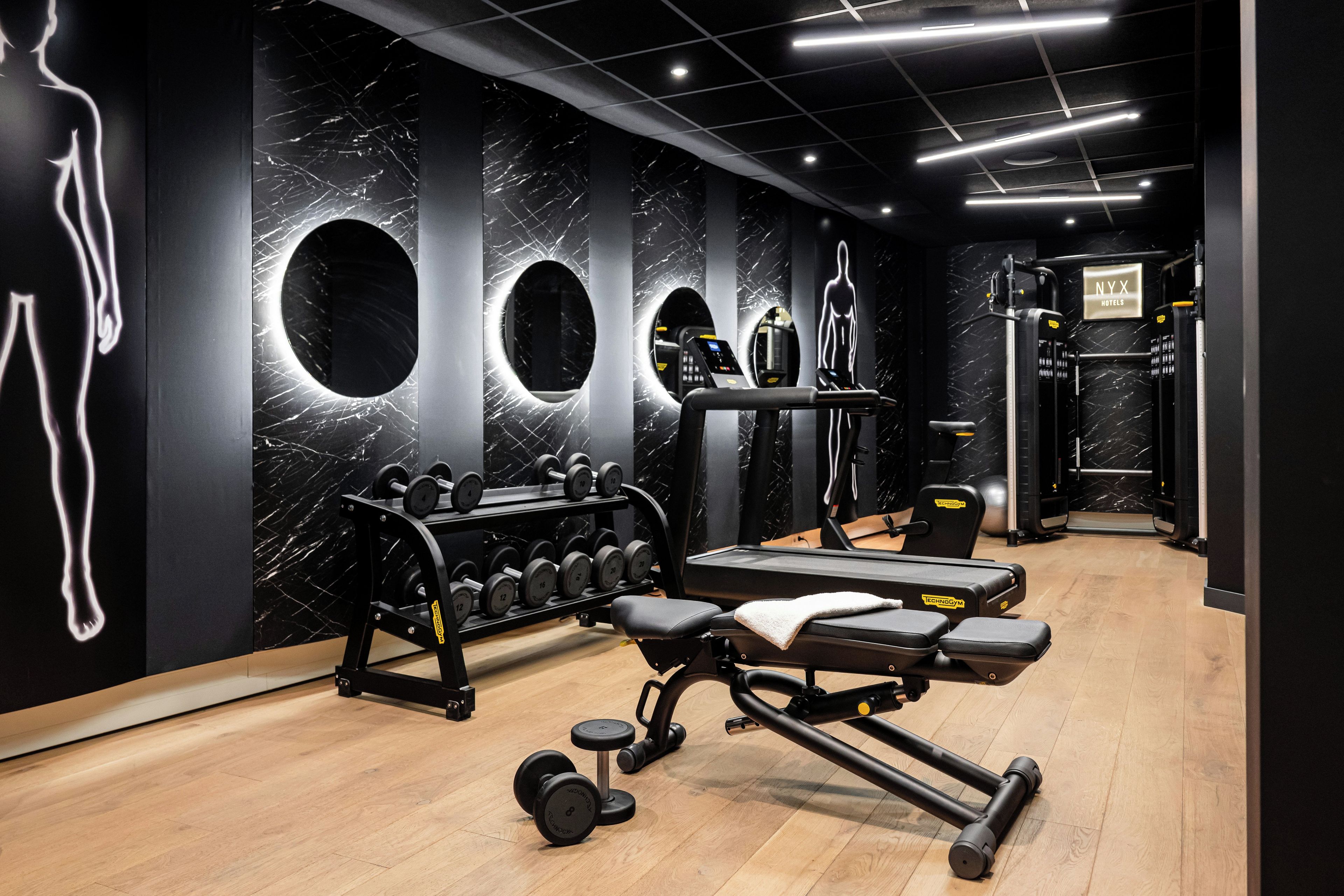 Ein Fitnessraum mit Trainingsgeräten, Marmorwänden und einem Schild für NYX Hotels.