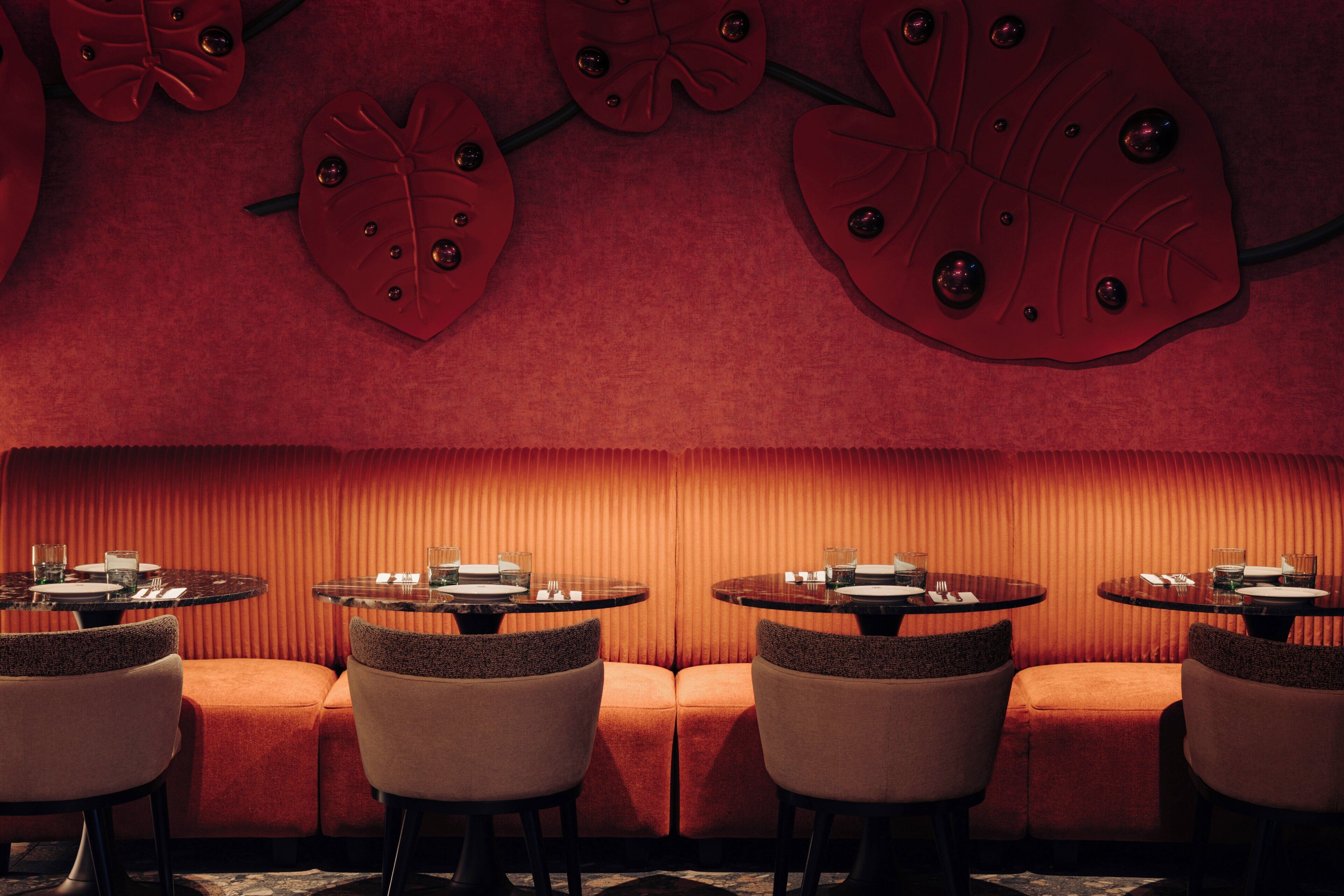 A restaurant with a red interior, round tables, and cushioned seating.