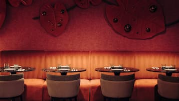 A restaurant with a red interior, round tables, and cushioned seating.