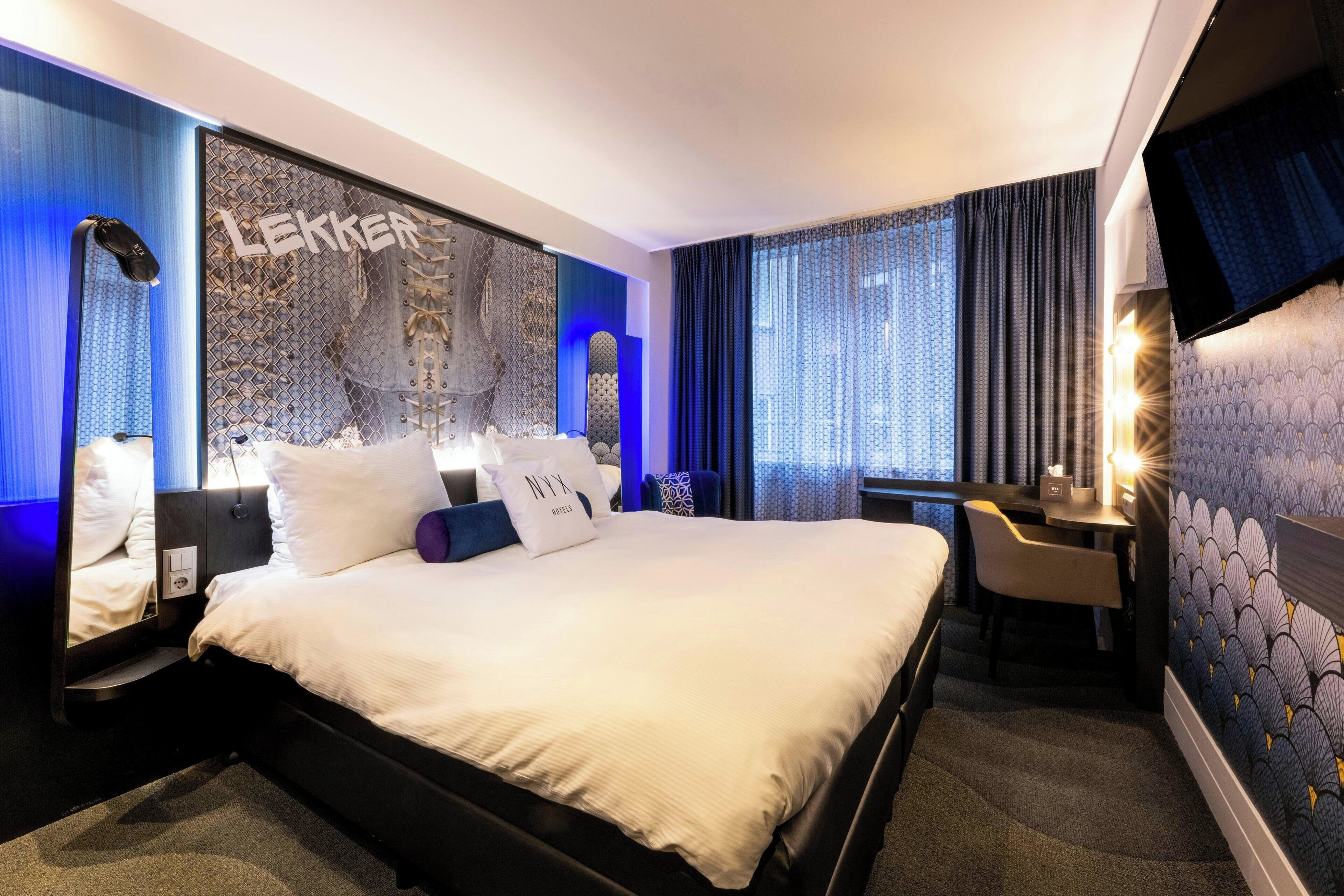A hotel room with a large bed, a desk, and a TV mounted on the wall.