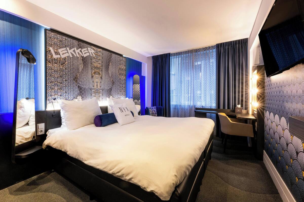 A hotel room with a large bed, a desk, and a TV mounted on the wall.