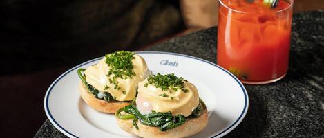 A plate with two eggs benedict sandwiches and a glass of tomato juice with a straw.