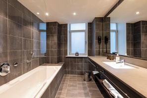 A modern bathroom with a bathtub, two sinks, a vanity, and a large mirror. - NYX Hotel Amsterdam Rembrandt Square (Amsterdam)