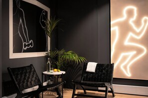 Quarto com duas cadeiras de fibra preta, uma mesinha redonda com uma garrafa e um copo, e um vaso de planta.